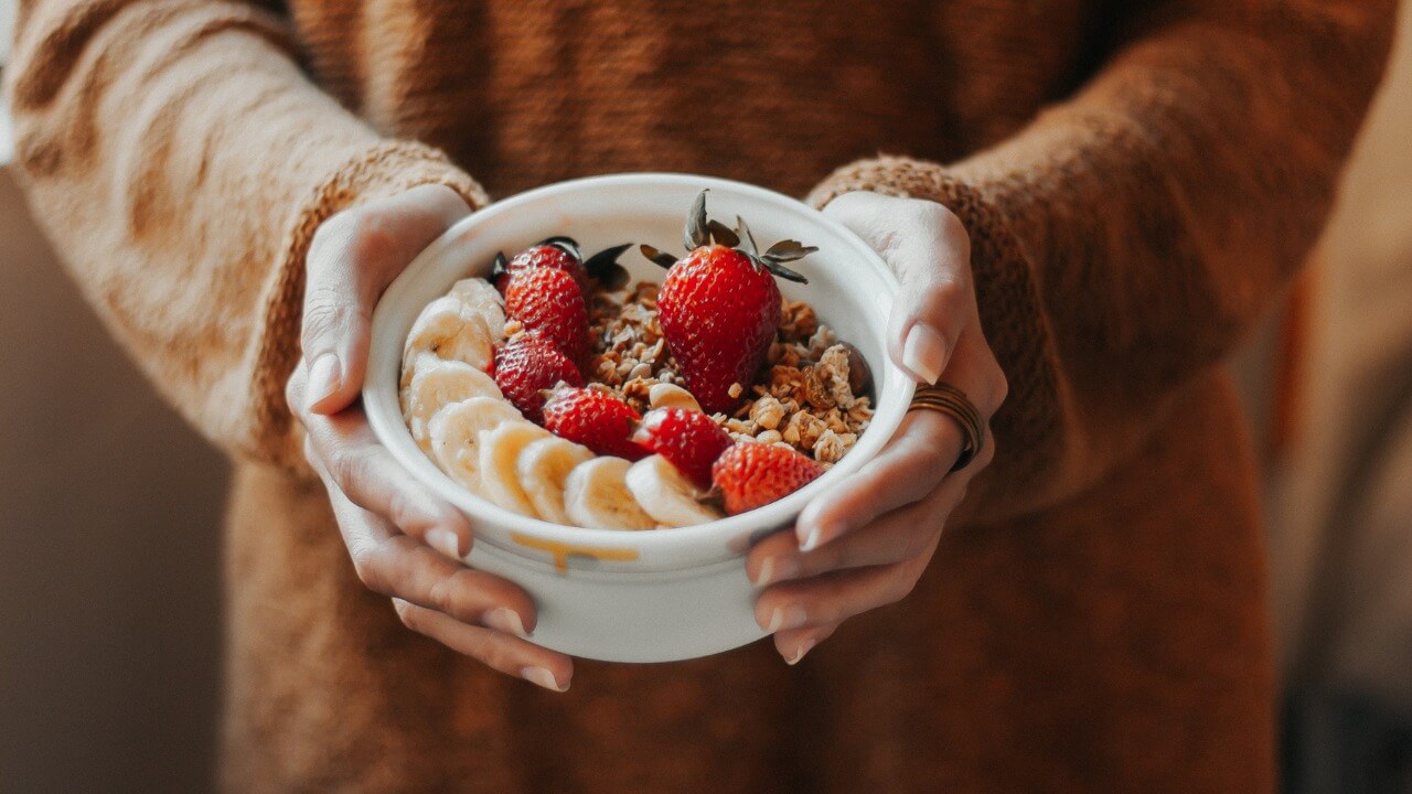 A person holding a breakfast bowl with oats and fruits.