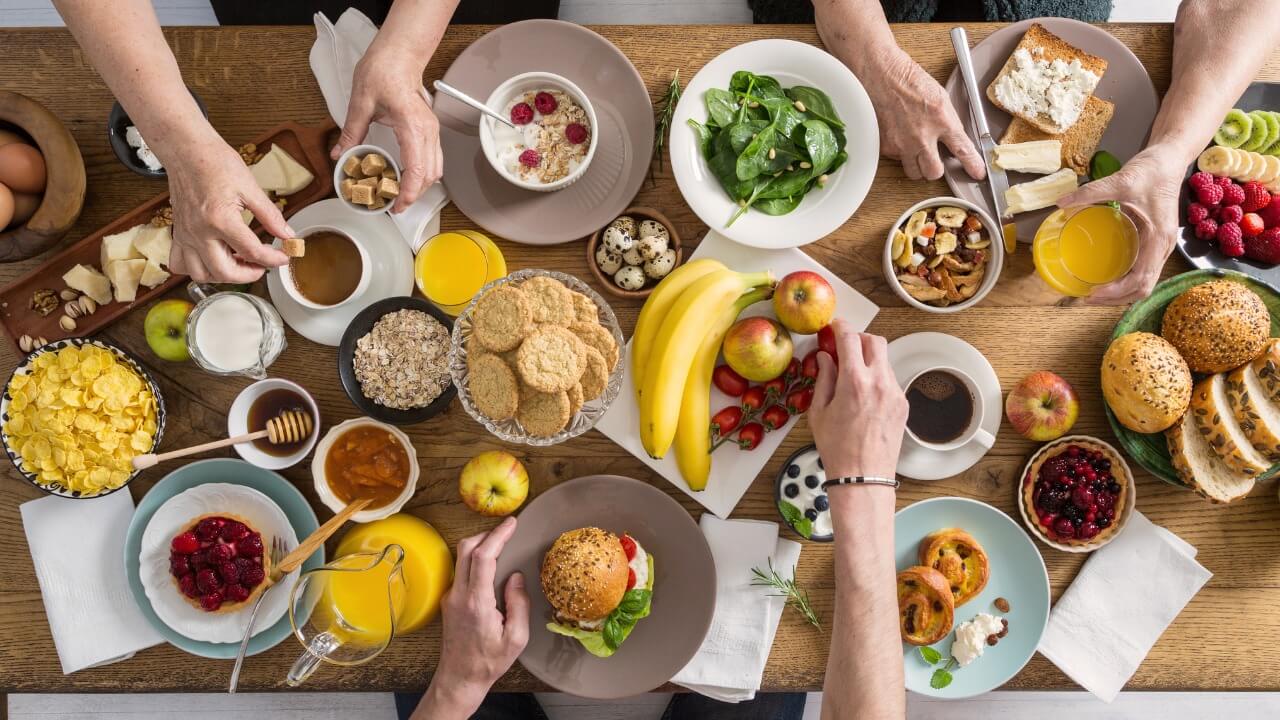 Overhead view of a table spread with different food items shared with different people.