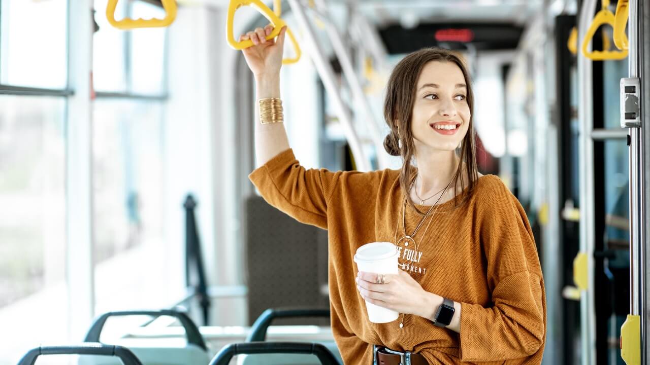 A female student on a bus holding a cup of coffee.
